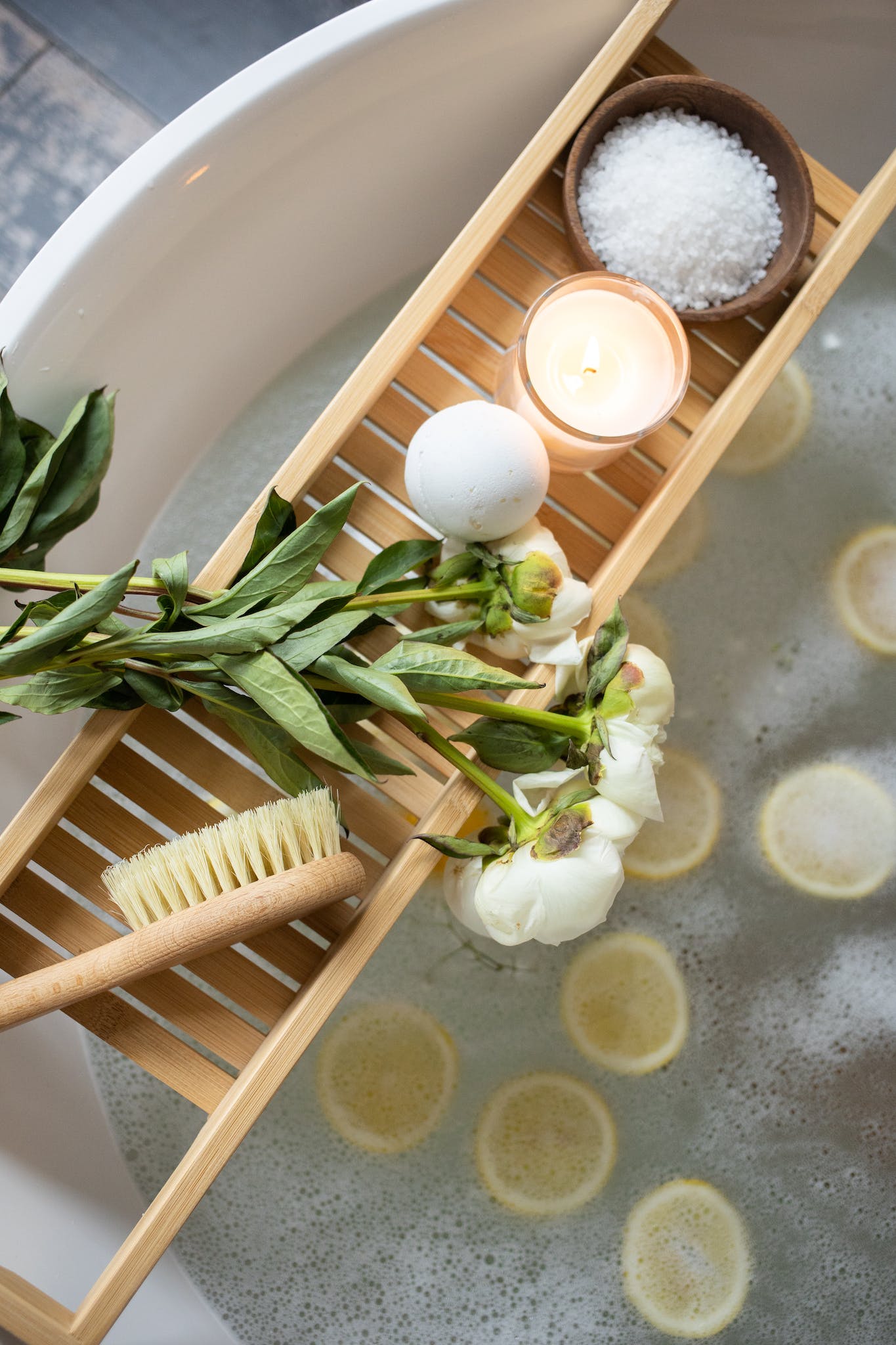 Top view of wooden tray with bath bomb and burning candle placed near salt and flowers on tub with lemon slices on water - How to Deal with Homesickness Abroad